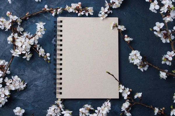 Notepad and Cherry branches with spring flowers on a dark blue background.