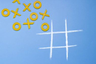 Sarı plastik haçlar ve bir ayak ve mavi bir arka plan üzerinde üç taş oynamak için çizgili bir alan. Kavram Xo kazanmak Challenge. Gelişimsel oyun çocuklar için. Düz yatıyordu, en iyi görünümü.