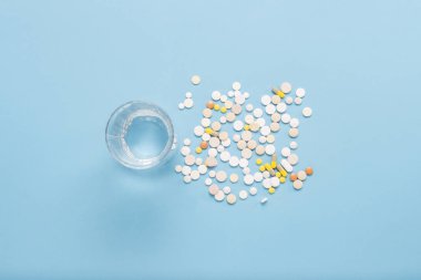 Bir bardak su ve çeşitli haplar mavi bir arka plan üzerinde. Hastalık ve hastalık halinde ilaçlar kavramı. Düz yatıyordu, en iyi görünümü.