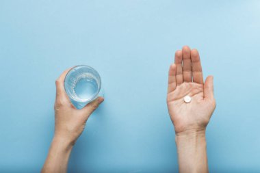 İkinci el Mavi bir arka plan üzerine bir bardak su tutarken el bir avuç hap tutuyor. Hastalık ve hastalık halinde ilaçlar kavramı. Düz yatıyordu, en iyi görünümü.