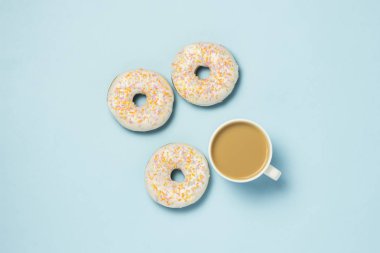 Fincan, kahve ya da çay süt ve taze lezzetli donuts mavi bir arka plan üzerinde beyaz. Fırın kavramı, taze hamur işleri, lezzetli breakfast, lokanta. Düz yatıyordu, en iyi görünümü