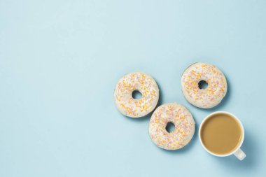 Fincan, kahve ya da çay süt ve taze lezzetli donuts mavi bir arka plan üzerinde beyaz. Fırın kavramı, taze hamur işleri, lezzetli breakfast, lokanta. Düz yatıyordu, en iyi görünümü