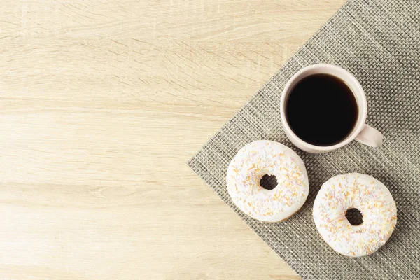 Tasty, sweet, fresh donuts and a cup with black coffee on the wooden background. Breakfast concept, fast food, coffee shop, bakery