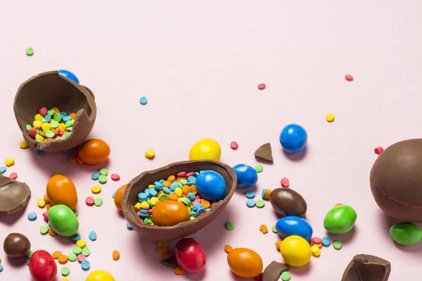 Broken and whole chocolate Easter eggs, multicolored sweets ,pink background. Shrub. Concept of celebrating Easter, Easter decorations. Flat lay, top view. Copy Space. Happy Easter