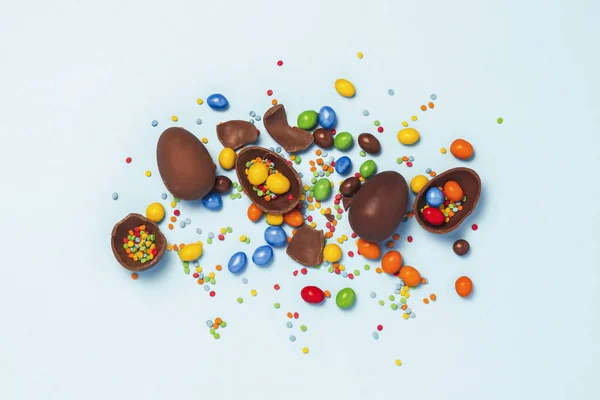 破碎和整个巧克力复活节彩蛋 在蓝色背景上的五颜六色的糖果 庆祝复活节 复活节装饰的概念 寻找复活节兔子糖果 平坦的平面 顶部的景色 复制空间 — 图库照片