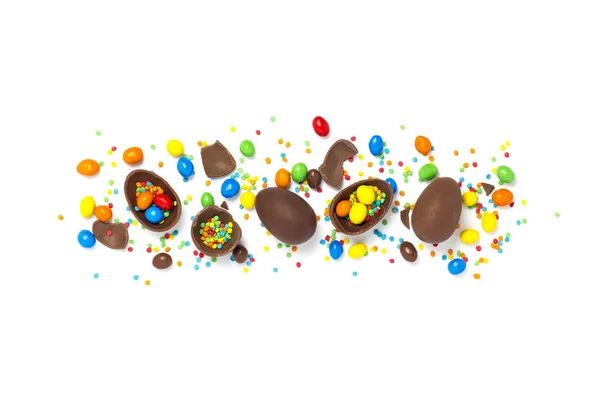 Broken and whole chocolate Easter eggs, multicolored sweets on white background. Concept of celebrating Easter, Easter decorations, search for sweets for Easter Bunny. Flat lay, top view. Copy Space