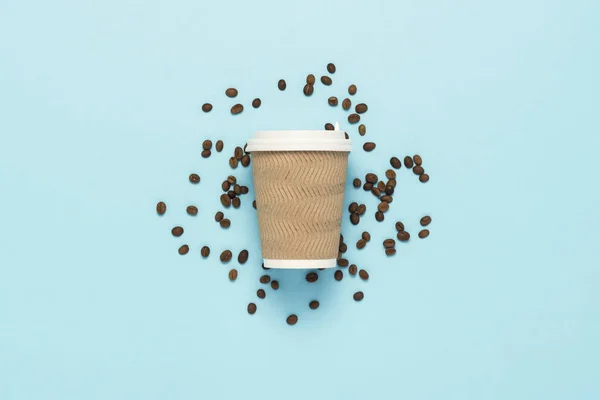 Disposable paper cup with a plastic lid for hot coffee or tea on a blue background with grains of coffee. Flat lay, top view