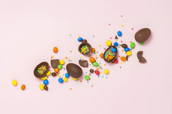 Broken and whole chocolate Easter eggs, multicolored sweets ,pink background. Shrub. Concept of celebrating Easter, Easter decorations. Flat lay, top view. Copy Space. Happy Easter