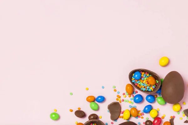 Broken and whole chocolate Easter eggs, multicolored sweets ,pink background. Shrub. Concept of celebrating Easter, Easter decorations. Flat lay, top view. Copy Space. Happy Easter