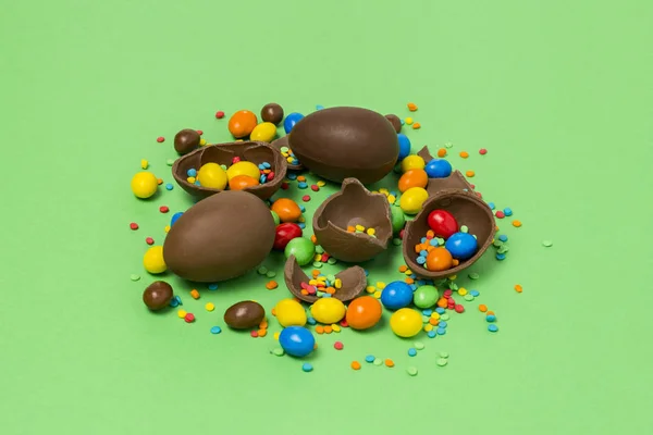 Broken and whole chocolate Easter eggs, multicolored sweets ,green background. Shrub. Concept of celebrating Easter, Easter decorations. Flat lay, top view. Copy Space. Happy Easter