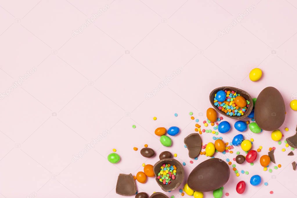 Broken and whole chocolate Easter eggs, multicolored sweets ,pink background. Shrub. Concept of celebrating Easter, Easter decorations. Flat lay, top view. Copy Space. Happy Easter