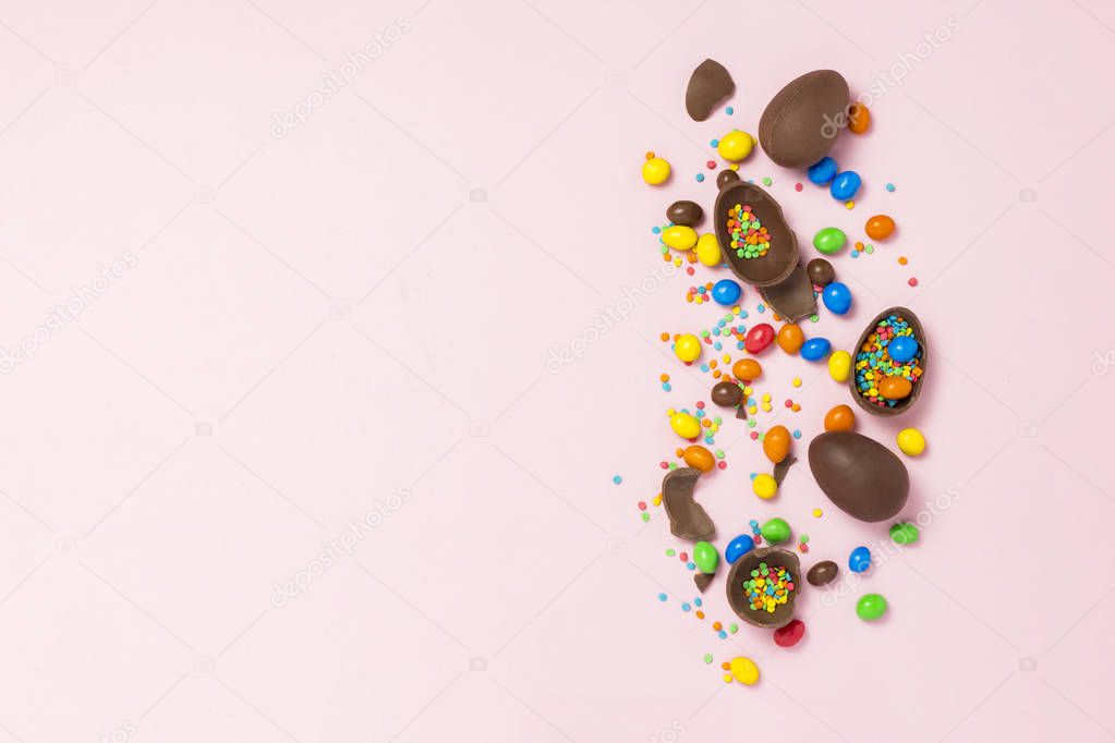 Broken and whole chocolate Easter eggs, multicolored sweets ,pink background. Shrub. Concept of celebrating Easter, Easter decorations. Flat lay, top view. Copy Space. Happy Easter
