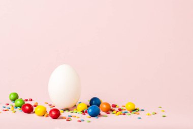 Beyaz Paskalya yumurtası ve pembe bir arka plan üzerinde çok renkli tatlılar. Paskalya kutlamaları kavramı
