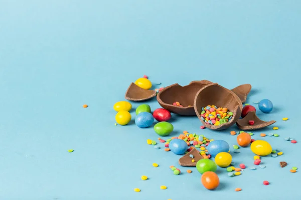破碎的巧克力复活节彩蛋和五颜六色的糖果在蓝色的背景 复活节庆祝概念 — 图库照片
