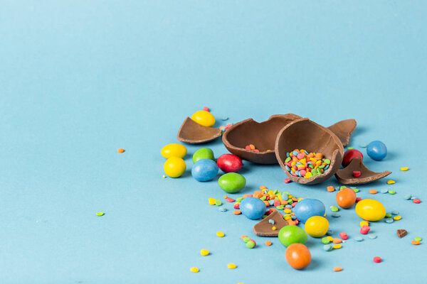 Broken Chocolate Easter Egg and multicolored sweets on a blue background. Easter celebration concept