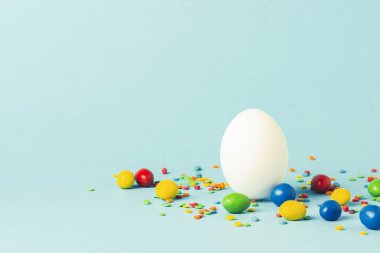 Beyaz Paskalya yumurtası ve mavi bir arka plan üzerinde çok renkli tatlılar. Paskalya kutlamaları kavramı