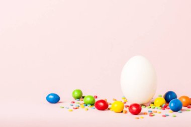 Beyaz Paskalya yumurtası ve pembe bir arka plan üzerinde çok renkli tatlılar. Paskalya kutlamaları kavramı