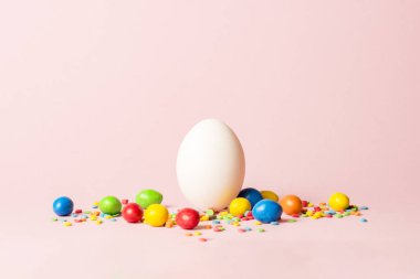 Beyaz Paskalya yumurtası ve pembe bir arka plan üzerinde çok renkli tatlılar. Paskalya kutlamaları kavramı
