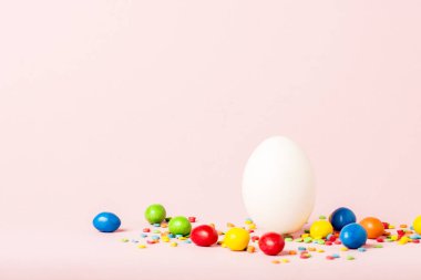 Beyaz Paskalya yumurtası ve pembe bir arka plan üzerinde çok renkli tatlılar. Paskalya kutlamaları kavramı