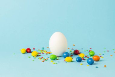 Beyaz Paskalya yumurtası ve mavi bir arka plan üzerinde çok renkli tatlılar. Paskalya kutlamaları kavramı