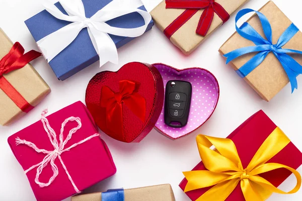 Open red gift box heart with car keys on a white background with gift boxes. Car gift concept, a surprise for a loved one. Flat lay, top view