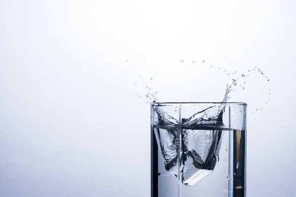 A splash of water in a glass from an ice cube on a white background. The concept of quenching thirst and cooling drinks in hot weather. Water balance and daily water consumption