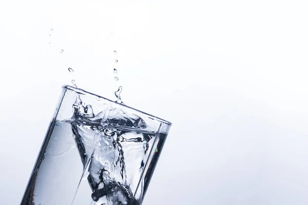 A splash of water in a glass from an ice cube on a white background. The concept of quenching thirst and cooling drinks in hot weather. Water balance and daily water consumption