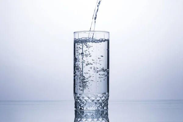 Glass is filling with a stream of clean and refreshing water on a white background. Concept of quenching thirst and cooling drinks in hot weather. Water balance and daily water consumption