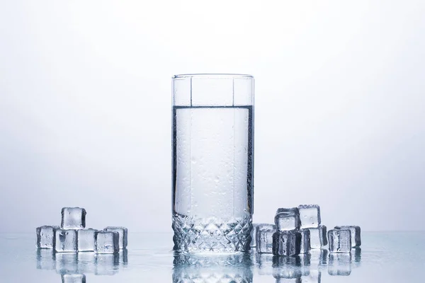 A glass of clean refreshing water and ice cubes on a white background. The concept of quenching thirst and cooling drinks in hot weather. Water balance and daily water consumption