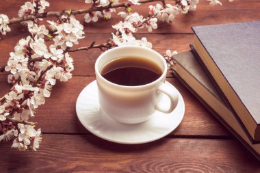Sakura dalları çiçekler, beyaz fincan siyah kahve ve koyu ahşap arka plan üzerinde iki kitap ile. Bahar kavramı