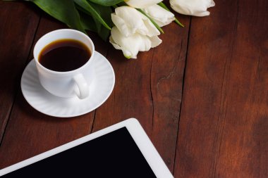 Lale, bir fincan kahve ve bir tablet koyu ahşap arka plan üzerinde beyaz. Bahar kavramı