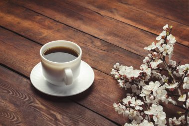 Sakura dalları çiçek ve koyu ahşap arka plan üzerinde koyu bir kahve ile beyaz bir fincan ile. Bahar kavramı