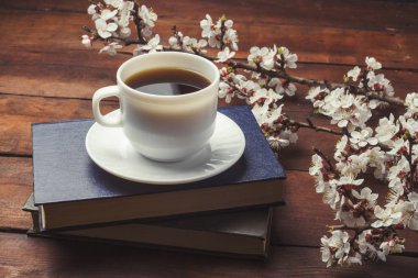 Sakura dalları çiçekler, beyaz fincan siyah kahve ve koyu ahşap arka plan üzerinde iki kitap ile. Bahar kavramı