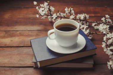 Sakura dalları çiçekler, beyaz fincan siyah kahve ve koyu ahşap arka plan üzerinde iki kitap ile. Bahar kavramı