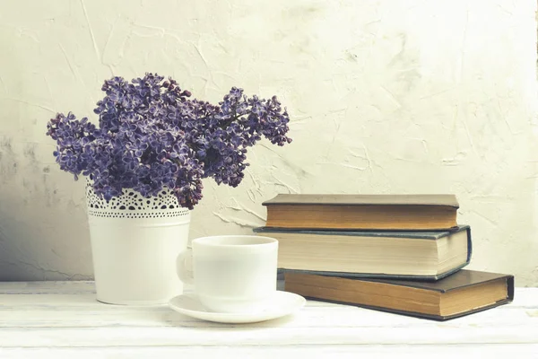 Lilás em balde decorativo branco, pilha de livros, copo branco com café sobre fundo de pedra branca — Fotografia de Stock