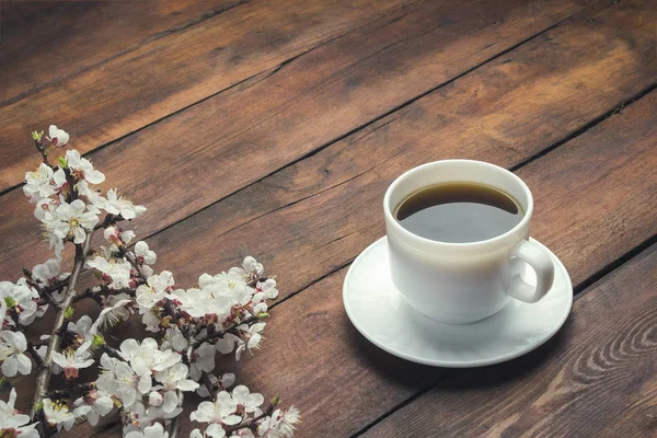 Sakura ágak, virágok és egy fehér csésze, egy fekete kávé, sötét fából készült háttér előtt. Tavaszi fogalmának — Stock Fotó