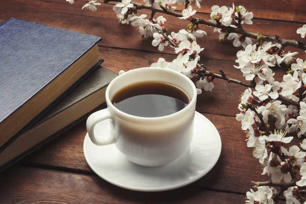 Sakura ramos com flores, xícara branca com café preto e dois livros em um fundo de madeira escura. Conceito de Primavera — Fotografia de Stock