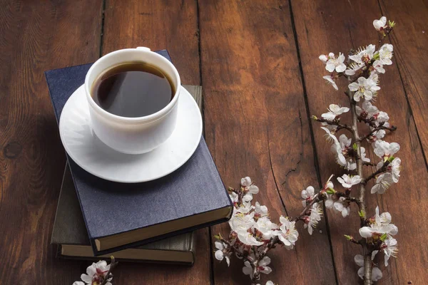 Sakura ramos com flores, xícara branca com café preto e dois livros em um fundo de madeira escura. Conceito de Primavera — Fotografia de Stock