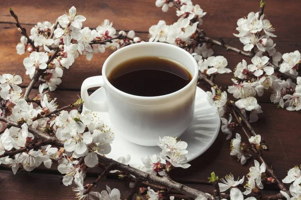 Sakura ágak, virágok és egy fehér csésze, egy fekete kávé, sötét fából készült háttér előtt. Tavaszi fogalmának — Stock Fotó