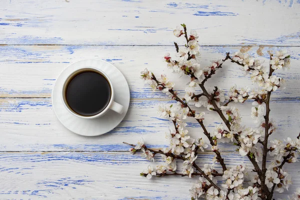Ágacska cseresznye virágok és a fehér csésze fekete kávé a fehér fa háttér. Lapos feküdt, top view. — Stock Fotó
