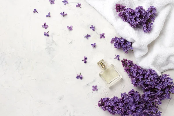 White towel, perfume bottle, lilac flowers on a white background. Top view, flat, lay, copy space.