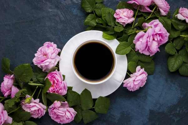 Fehér csésze fekete kávé és rózsaszín rózsa-sötét kék háttérrel. Lapos feküdt, top view — Stock Fotó