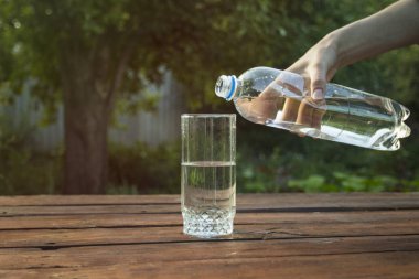 El bir bahar bahçe ahşap bir masa üzerinde bir bardak içine bir plastik şişe su dökülen