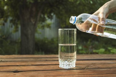 El bir bahar bahçe ahşap bir masa üzerinde bir bardak içine bir plastik şişe su dökülen