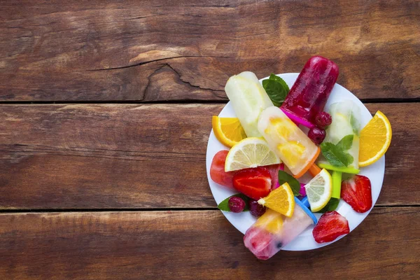 Homemade colorful, fruit popsicle, Fresh fruit on a white plate and a dark wooden background. Strawberry, Lemon, Lemon with mint, Orange, Cherry, Multifruit. Flat lay, top view — Stock Photo, Image