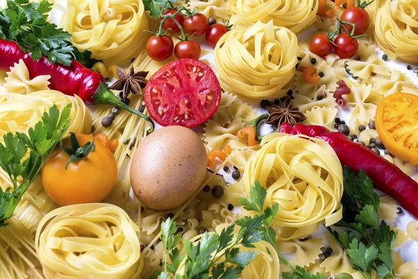 様々 なスパイス、赤唐辛子、鶏の卵、白地に黄色と赤のトマトのイタリアンのパスタ。イタリアンのパスタとソースの料理のコンセプト — ストック写真
