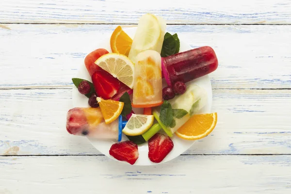 Homemade colorful, fruit popsicle, Fresh fruit on a white plate light wooden background. Strawberry, Lemon, Lemon with mint, Orange, Cherry, Multifruit. Flat lay, top view