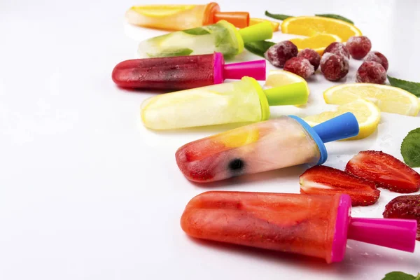 Multicolored bright fruit popsicle with strawberry, cherry, lemon, orange, lemon and mint and slices fresh fruit on a light white background