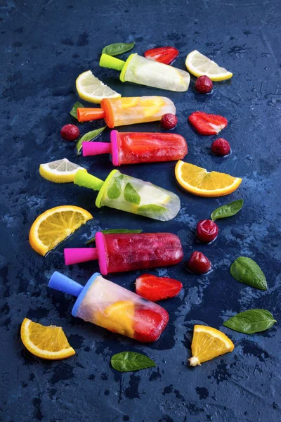 Homemade bright fruit popsicle with strawberry, cherry, lemon, orange, lemon and mint flavor and fresh fruit for ice cream on a dark blue background — Stock Photo, Image