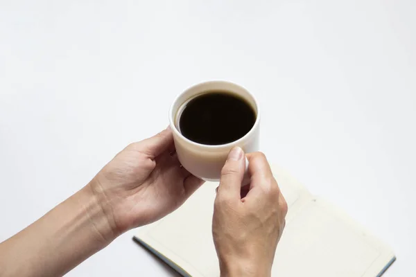 Kvinnliga händer håller en kopp svart kaffe och en öppen dagbok med rena sidor, en penna på en ljus bakgrund. Minimalistisk stil och kreativa koncept. Platt lekmanna, top view — Stockfoto